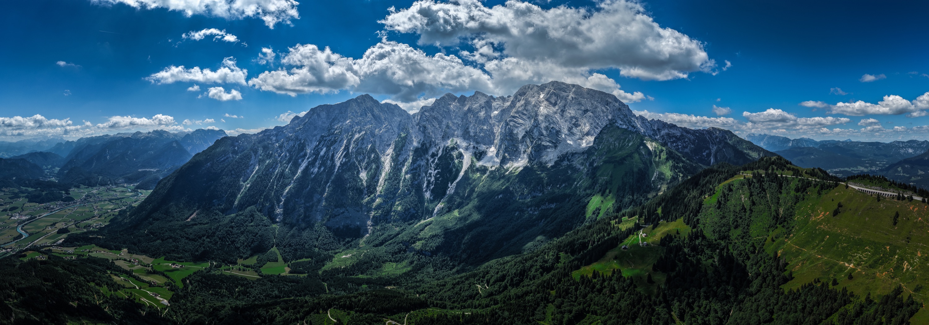 Wide aerial panorama of an Alpine mountain range beneath summer clouds
